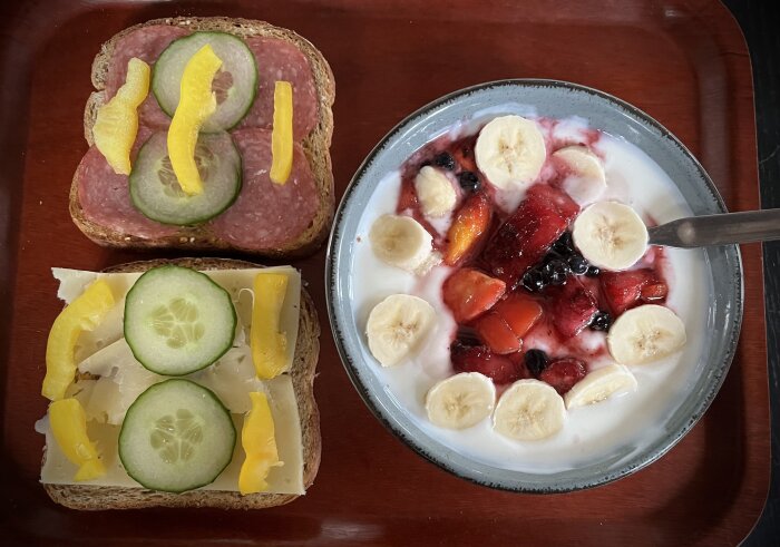 Mackor med ost, gurka, salami och paprika samt skål med yoghurt, banan och bär.