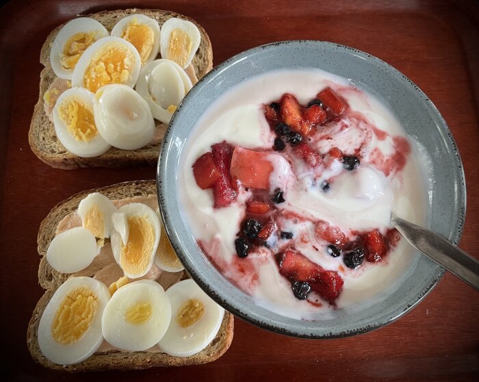 Skål med fil och bär samt mackor med kokt ägg på träbord, enkel måltid.