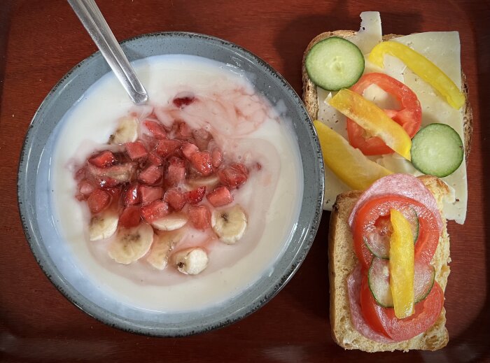 Frukost med fil och hackad frukt i en skål, macka med ost och grönsaker.