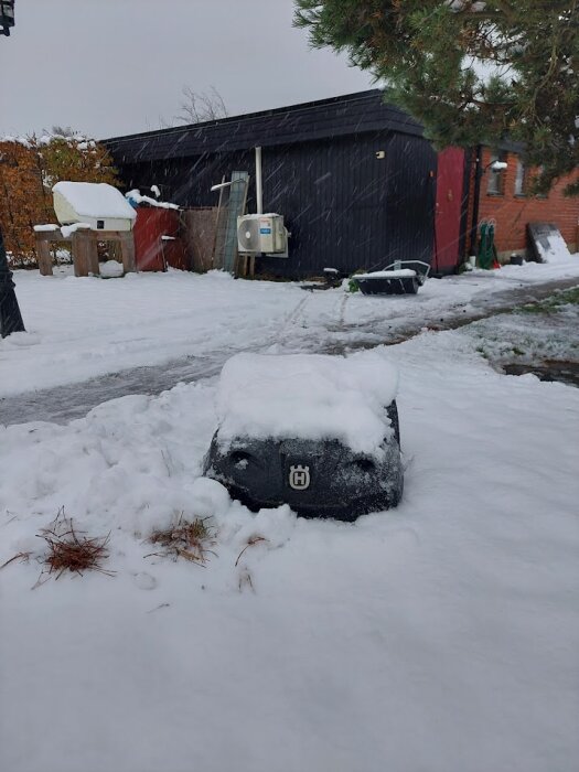 Robotgräsklippare täckt med snö framför ett hus och bildade föremål.