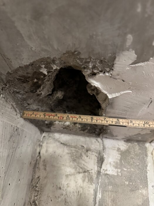 Bild av ett måttband framför ett ojämnt hål i betongtaket för ventilation i en lägenhetsrenovering.