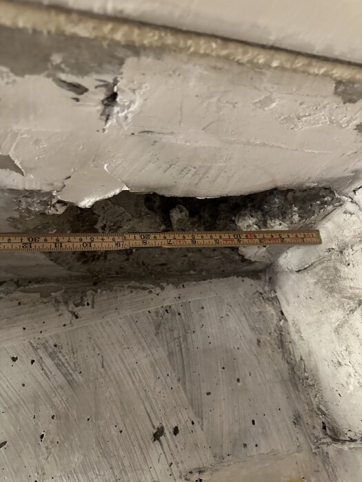 Mätning av ett hål i ett betongtak med en trälinjal, indikerar behov av anpassning för köksventilation.