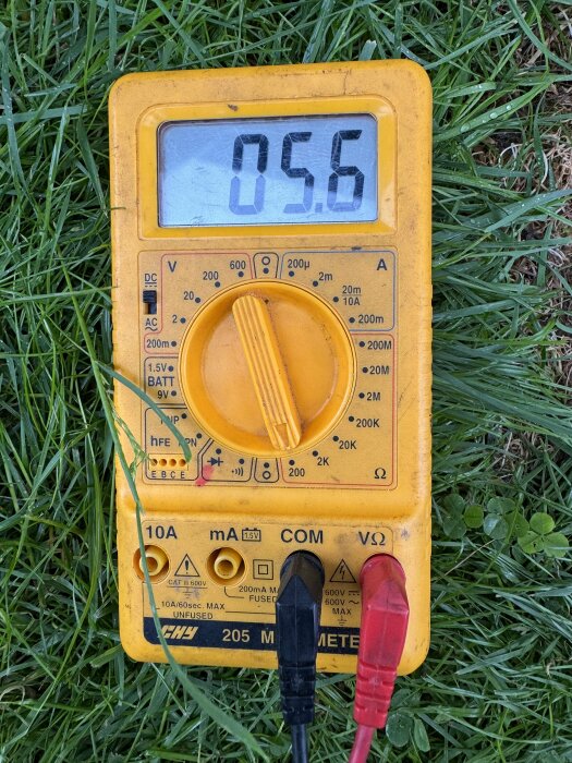 Multimeter på gräs visar 5.6 ohm, inkopplad med röd och svart testkabel.