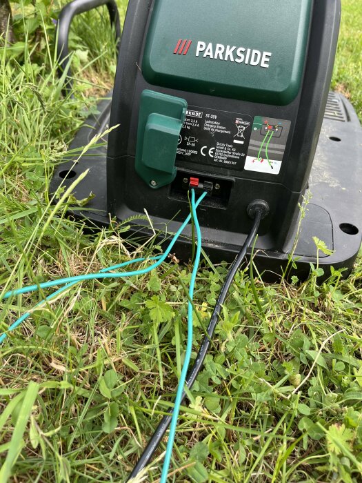 PARKSIDE-maskin på gräsmatta med öppet batterifack och trassliga guidetrådar som är inkopplade.
