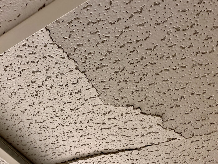 Närbild på en texturerad undertaksplatta med sprickor, möjligt innehåll av asbest från 60/70-talet.