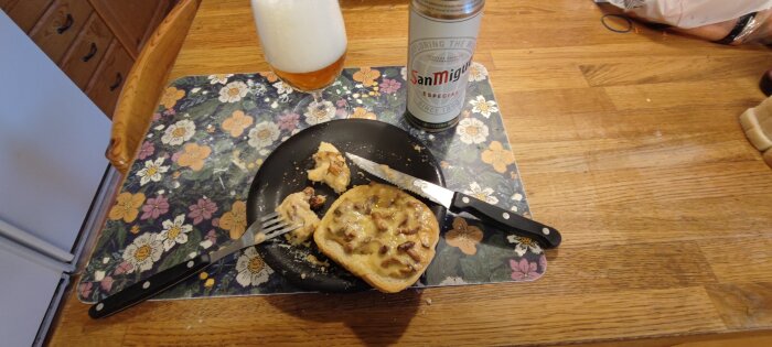 Toast med kantareller och Västerbotten ost, kniv, gaffel och San Miguel öl på blommigt bordstablett.