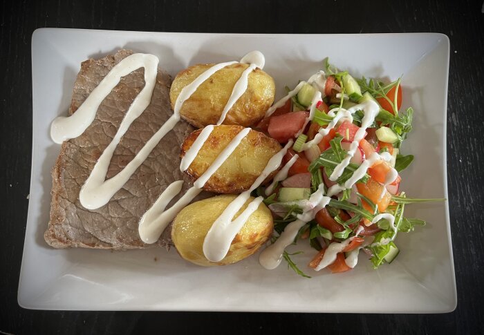 Middagstallrik med lövbiff, ugnsstekta potatishalvor och sallad toppad med dressing.