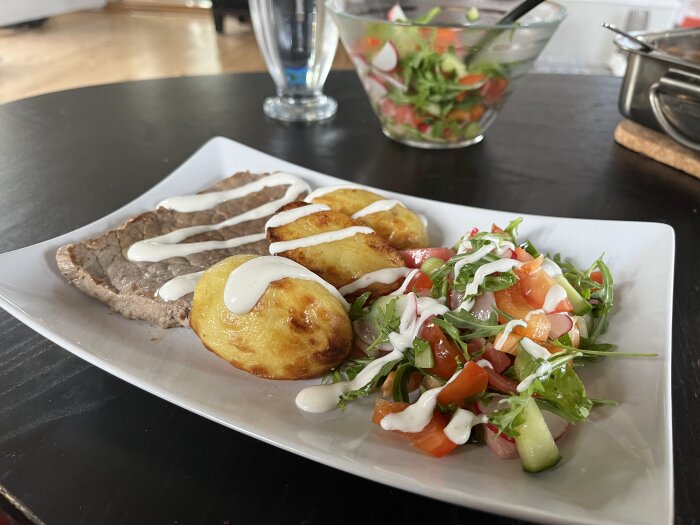 Måltid med lövbiff, ugnsstekta potatisar och fräsch sallad serverad på en vit tallrik.