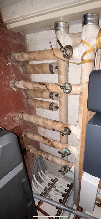 Äldre rördragning med isolerade vattenledningar och ventiler i ett pannrum.