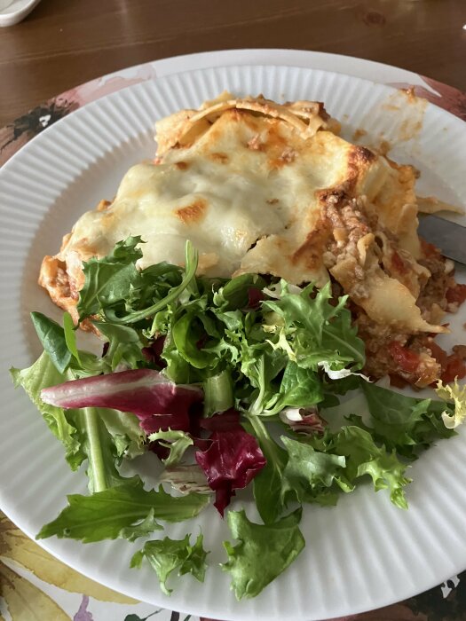 Portion av lasagne med smält ost och en sida av blandad grönsallad på en tallrik.