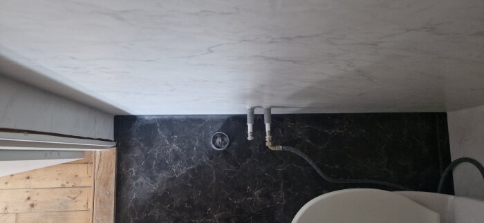 Förskjutna vatten- och avloppsrör över svart marmorbänkskiva och toalett i badrum under renovering.