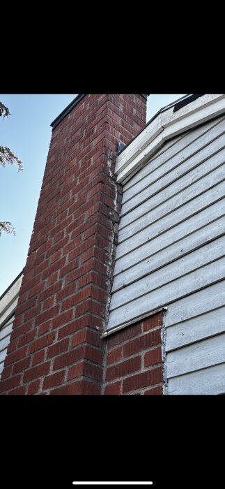 En spricka mellan en tegelskorsten och husets vita träpanel som tyder på sättning i utbyggnadsdel.