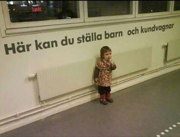 Barn står bredvid väggtext "Här kan du ställa barn och kundvagnar" i en butik.