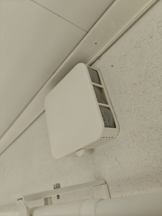 Väggventil monterad i hörnet av ett rum med synlig filter och ventilationskåpa i förgrunden.
