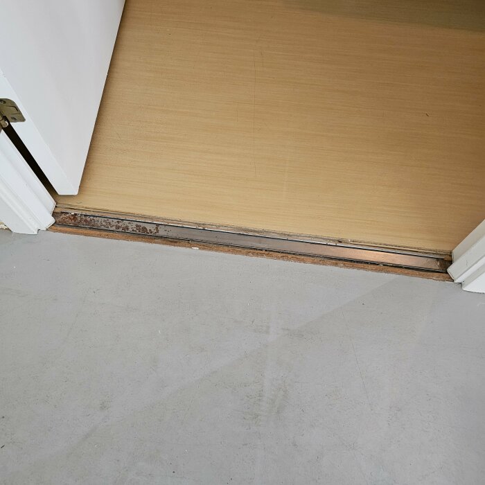 Golvövergång med grått klibbigt golv och parkett med nivålist vid en dörröppning.