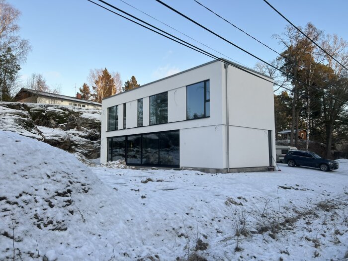 Modern villa med putsad lättbetongfasad, glaspartier och snötäckt mark.