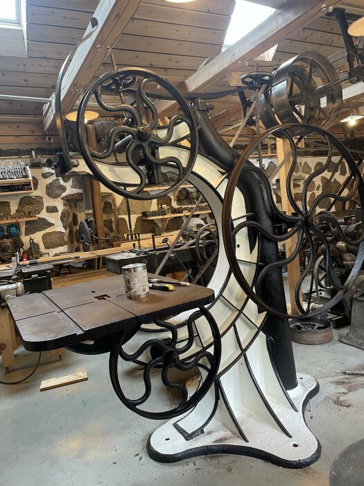 Renoverad historisk bandsåg från Jonsered med dekorativa hjul och nymålat bord i verkstadsmiljö.