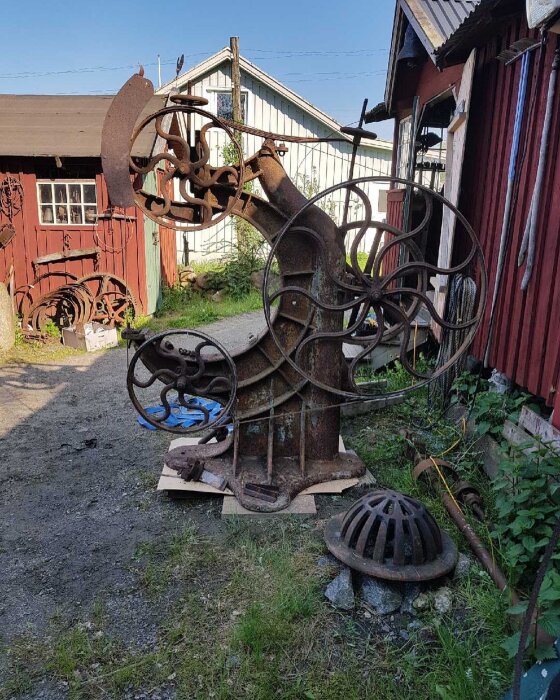 Renoverad, antik bandsåg från Jonsered med dekorativa hjul, står utomhus nära ladugård.