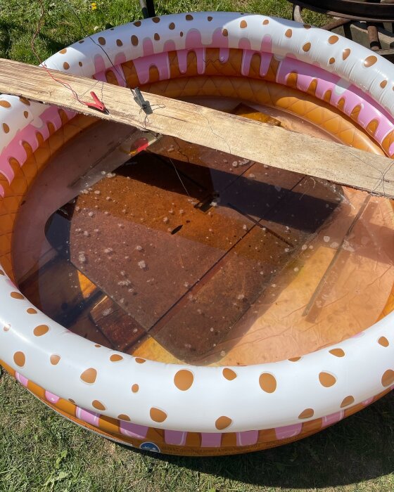 Träplankor i ett uppblåsbart barnbassäng fullt med vatten, använt för elektrolysbad i renoveringsprocess.