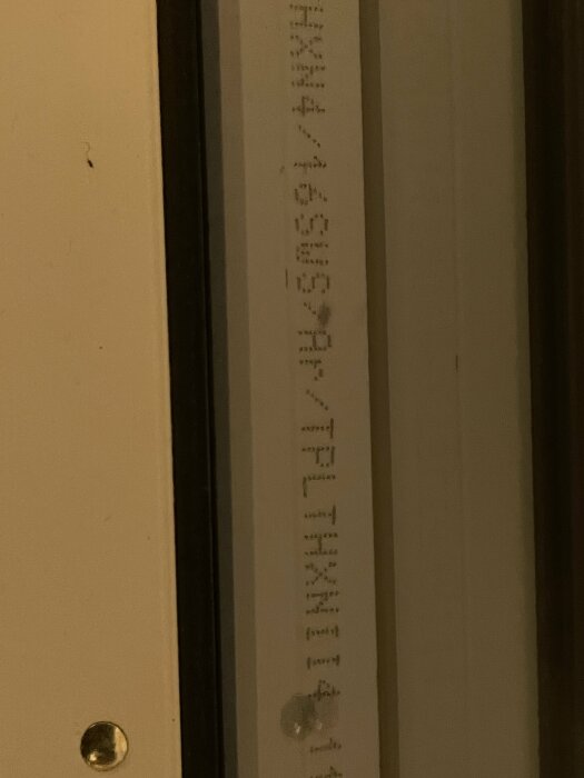 Närbild på en dörrkant med skriven text och mätmarkeringar, vilket indikerar storleken på en kassett.