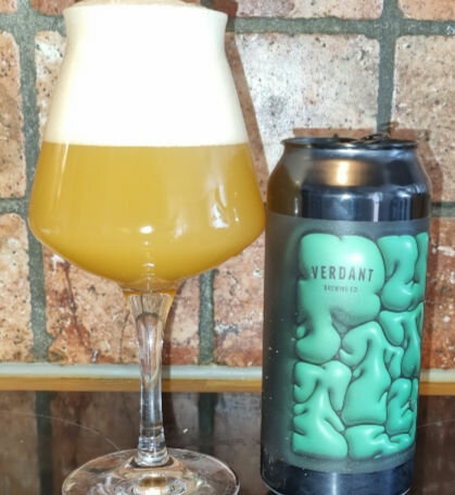 Ölglas fullt av skummande öl bredvid en ölburk från Verdant Brewing Co mot en tegelväggsbakgrund.