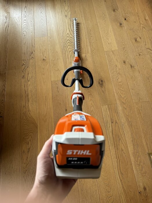 STIHL batteridriven stångsax som hålls i en hand framför ett trägolv.