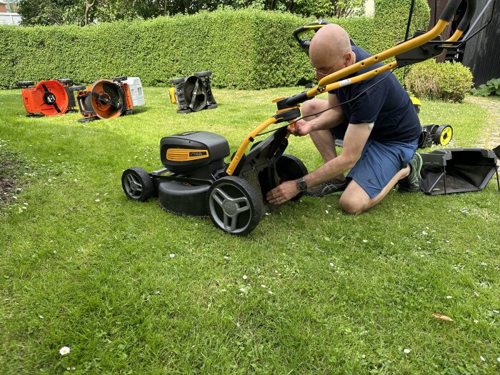 Person som justerar en gräsklippare på en gräsmatta med flera omkullvälta gräsklippare i bakgrunden.