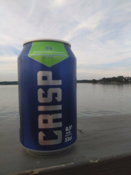Burk märkt "CRISP IPA" på en träbrygga med en sjö i bakgrunden.
