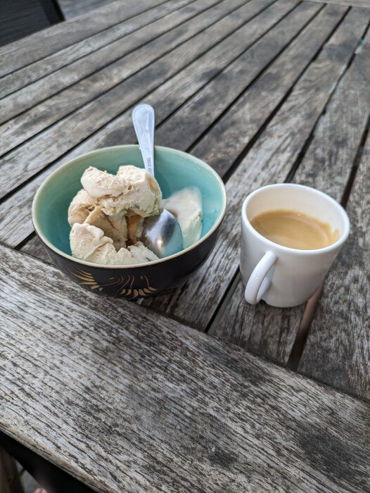 Skål med glass och sked samt en kopp kaffe på ett träbord utomhus.