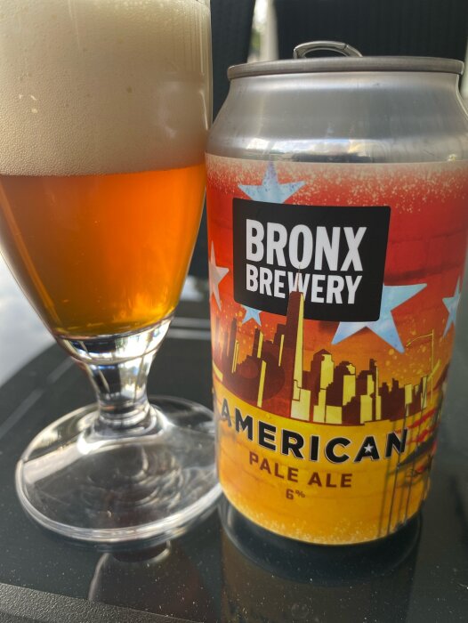 Ölglas med skummande ljus öl och en burk American Pale Ale från Bronx Brewery med synlig beska.