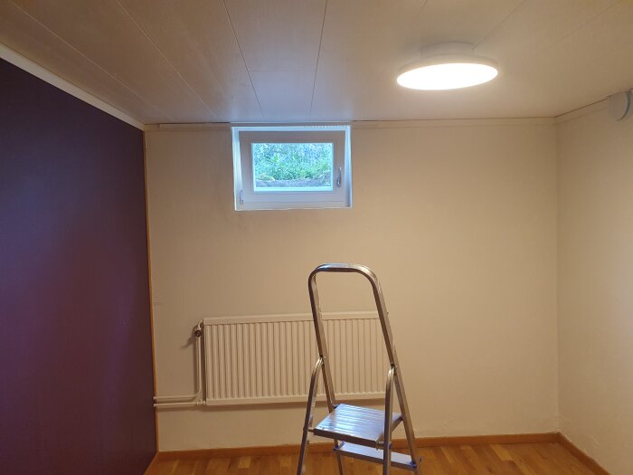 Nyinstallerat fönster i målat rum med stege, radiator och taklampa.