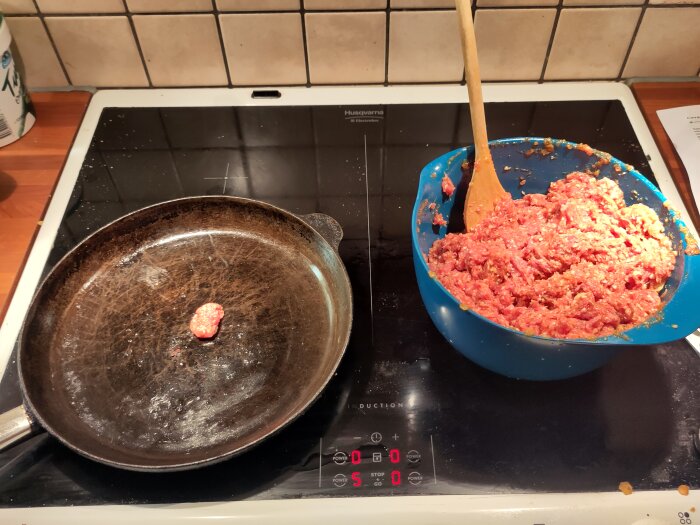 En stekpanna på spishäll och en skål med cevapi-smet och träslev på ett köksbänk.