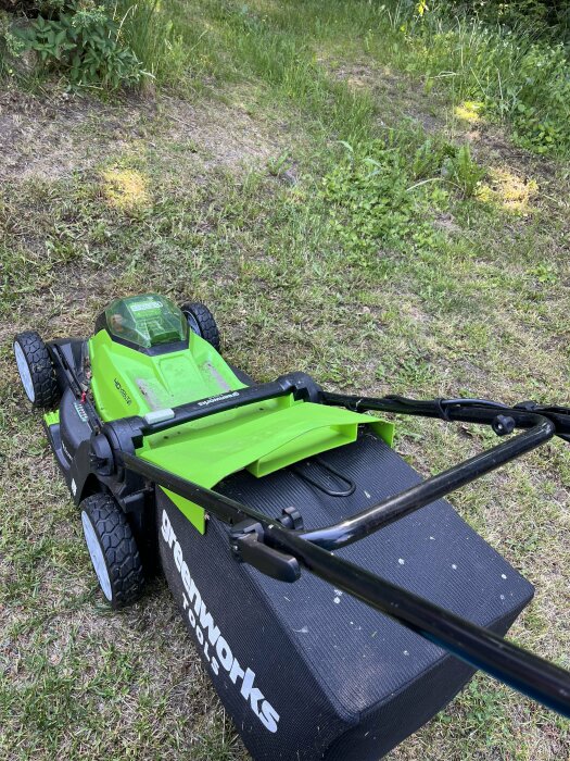 Grön eldriven gräsklippare med synligt batteri ute på en gräsmatta.