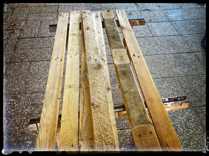 Gamla träpallar ligger på ett stenbelagt golv, redo för renoveringsprojekt.