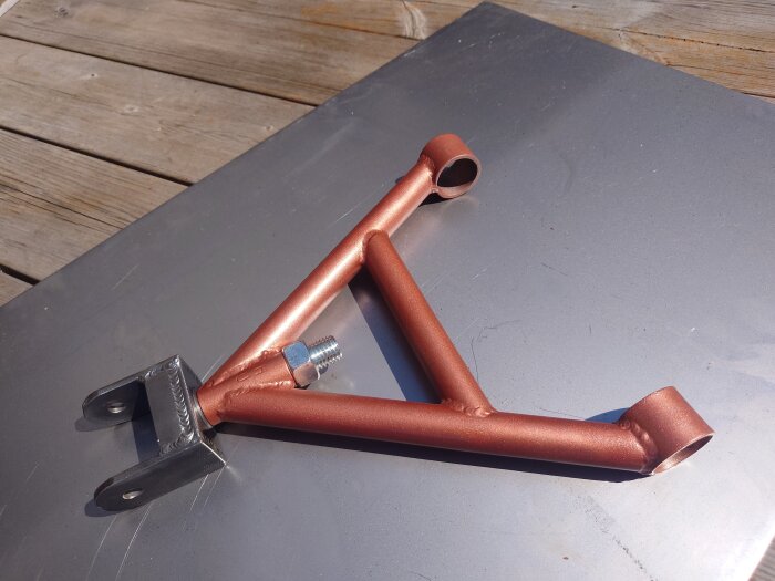Kopparfärgat metallfäste med bult på en grå plåt och träbakgrund.