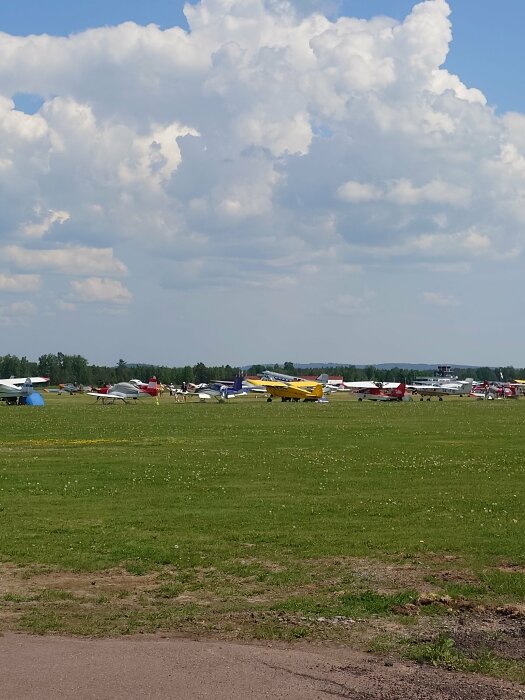 Flygplan parkerade på ett grönt fält med fluffiga moln på himlen i bakgrunden.