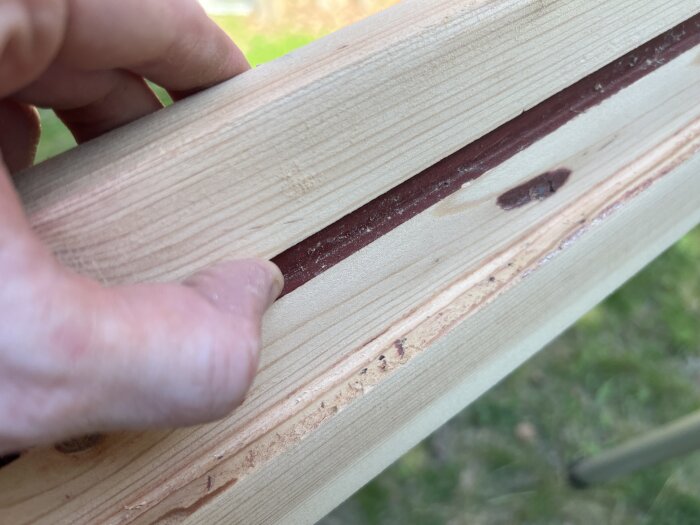 Slipad träkarm med synliga mörka spår och några pluggade hål, hand visar detalj.