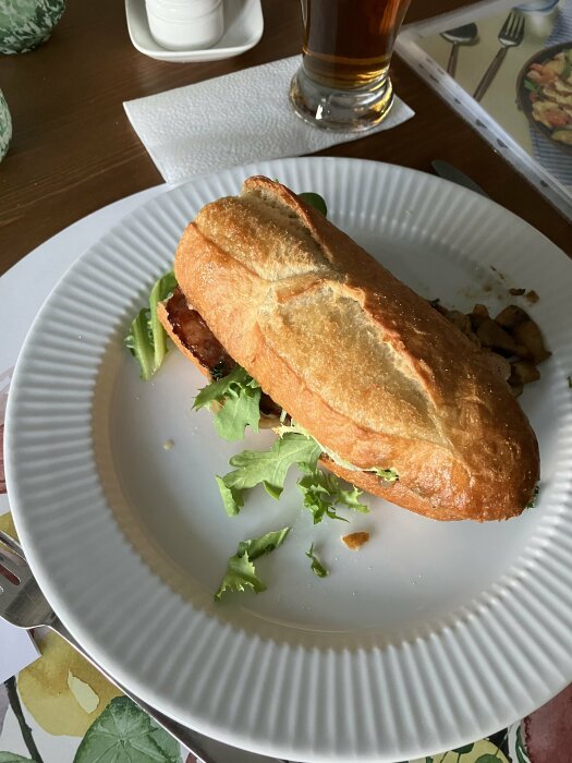 Baguette med bacon, svamp, lök och sallad på vit tallrik, persilje- och vitlöksdressing.