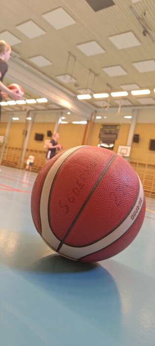 Basketboll nära kameran i en idrottshall med suddig bakgrund av spelare.