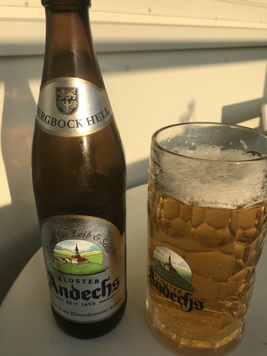 Flaska och glas av ölmärket Kloster Andechs på ett bord i solljus.