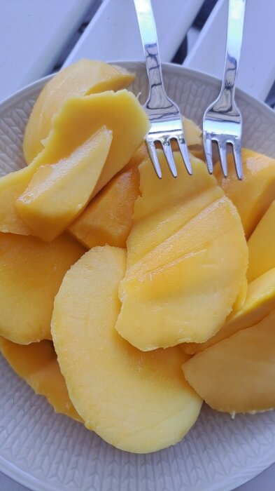 Skivad mango på en tallrik med två gafflar utomhus.