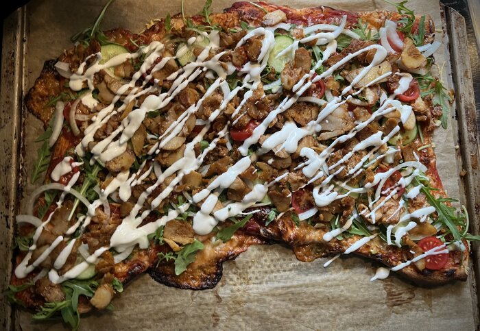 Hemgjord kebabpizza på bakplåtspapper med kyckling, sallad, tomat, vit sås och pincett-upplägg.