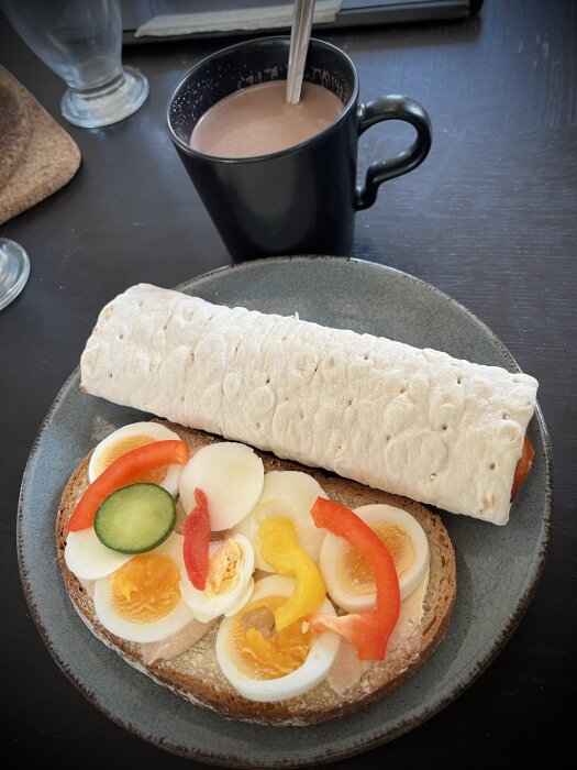 Frukost med rågbrödsmacka med ägg, grönsaker, kaviar, tunnbrödsrulle med skinka och grönt, kopp av choklad.