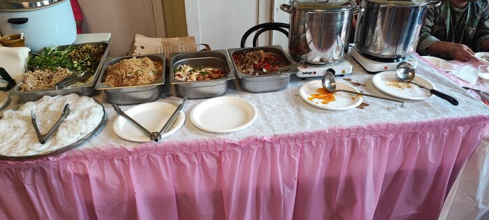 Buffébord med thairätter inklusive nudlar och grönsaker på en fest med rosa duk.