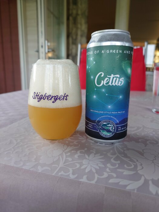 Ölglas med skum fyllt med öl märkt "Stigbergets" bredvid en burk "Cetus New England IPA" på bord.