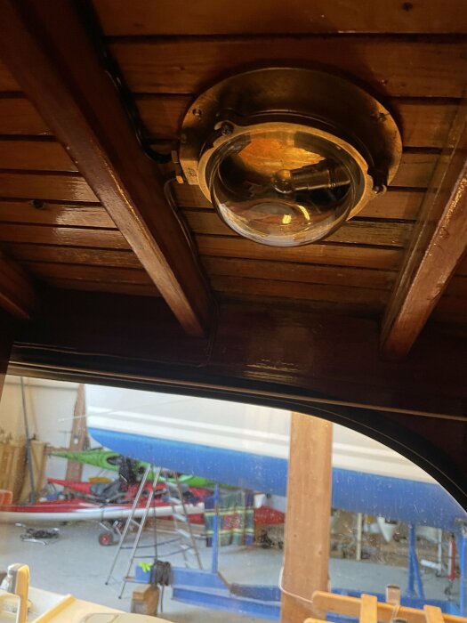 Ny mässingarmatur och klassisk strömbrytare monterade i mahognybåtens tak med arbetsplats i bakgrunden.