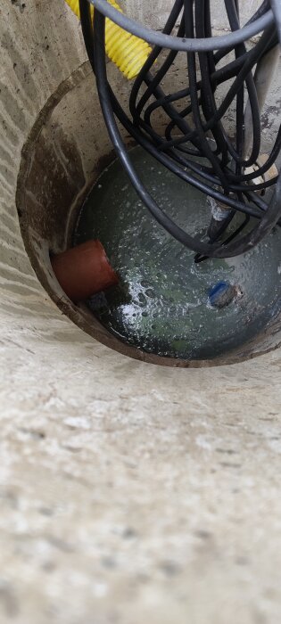 Grumligt vatten i en pumpbrunn med synliga kablar och en röd rörände.
