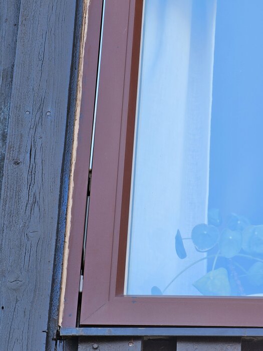 Närbild av ett fönster med brunt metallfönsterbleck som ser ut att sluttar inåt mot byggnadens tegelvägg.