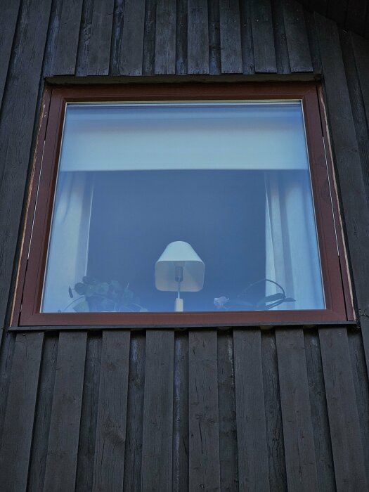 Fönster med brun metallkant på ett trähus, möjlig vattenskada vid karmen.