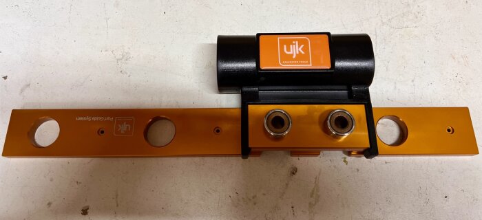UJK-märkt hålborrningsjigg med två orange linjaler och svart borrhållare avsedd för precision i MFT-bordstillverkning.